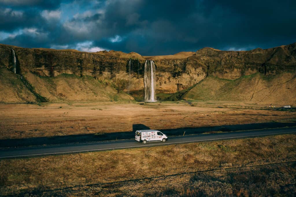 Camper van driving beside a waterfall in Iceland