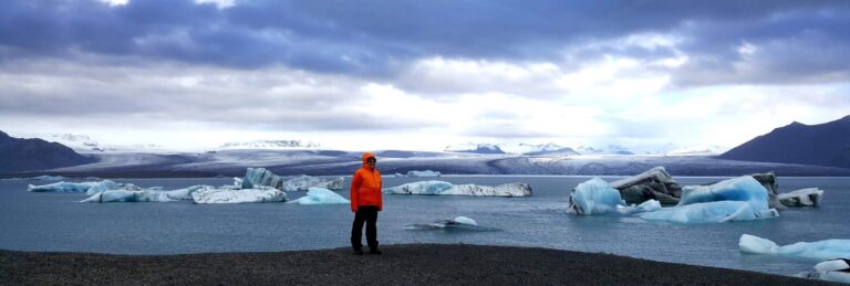 woman standing on a black beach in front of the glacier lagoon
