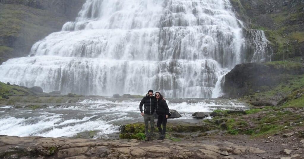 man and woman standing in front of dynjandi waterfall