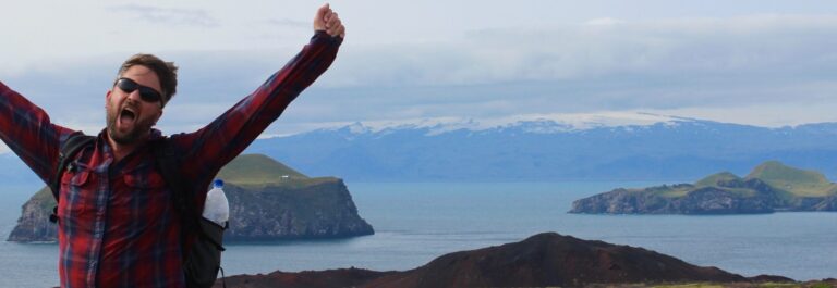 man holding out arms in front of heimaey close to westman islands