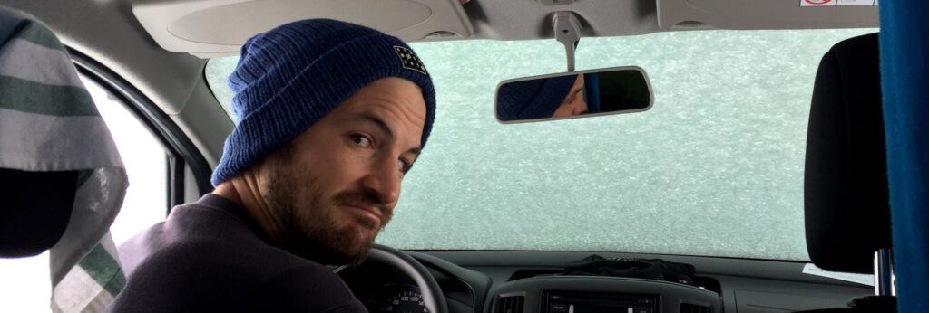 Man sitting inside camper van with window filled with snow