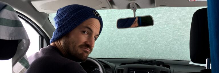 Man sitting inside camper van with window filled with snow