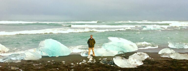 man standing on beach next to icebergs