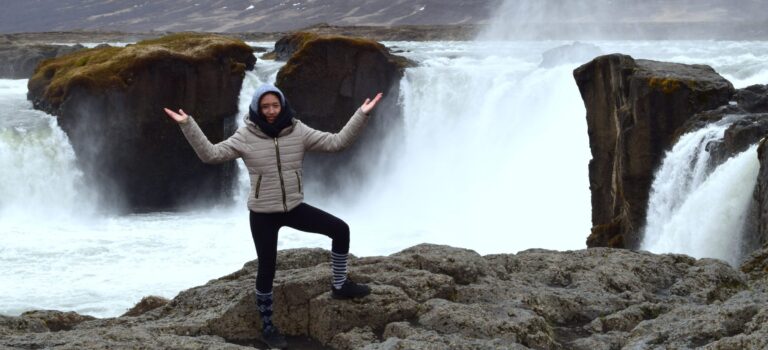 woman in front of waterfall raising hands