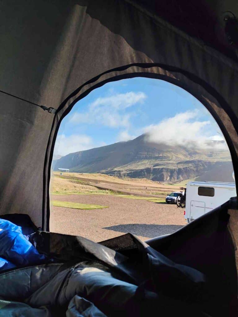 View from a tent placed on top if a Dacia Duster. The view is of a beautiful mountain and blue skies.