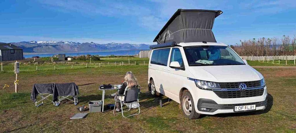 The VW California set up at campsite and a woman sitting at the camping table.