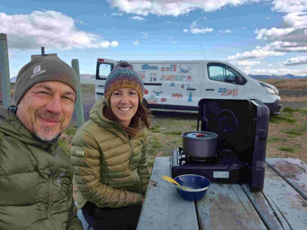 A couple cooking food on a picnic table next to a renault trafic