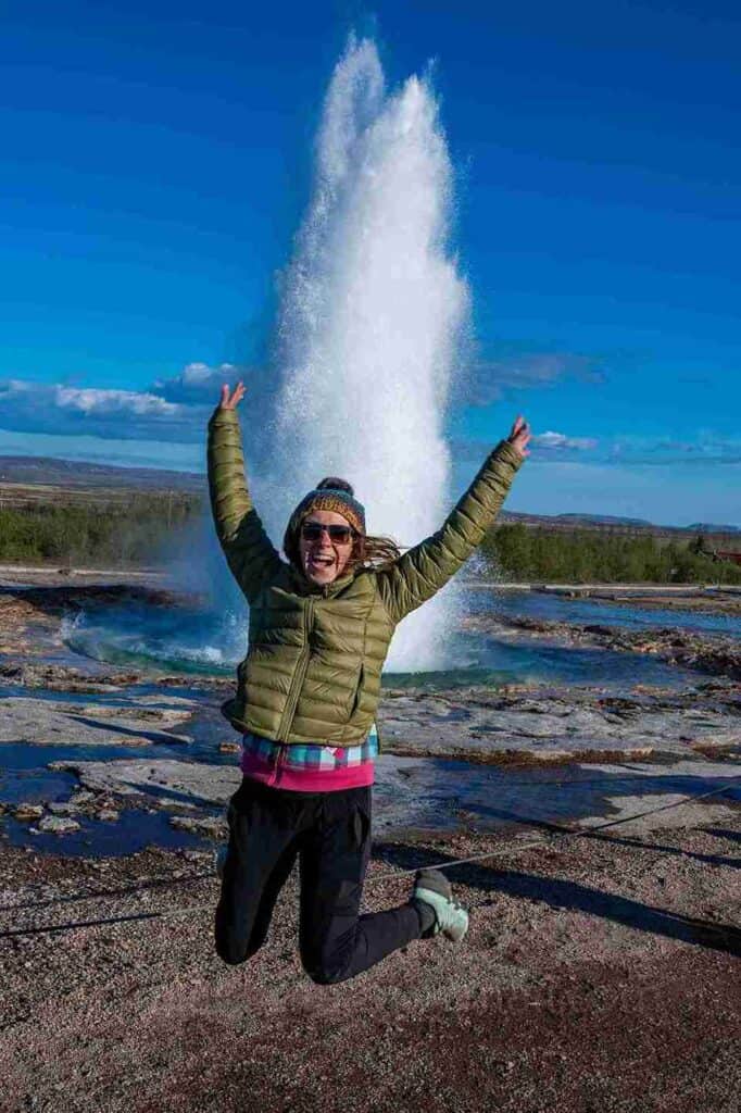 A woman jumping celebratory next to a Geysir.