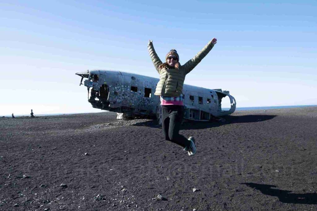 A woman jumping next to an old plain wreck.