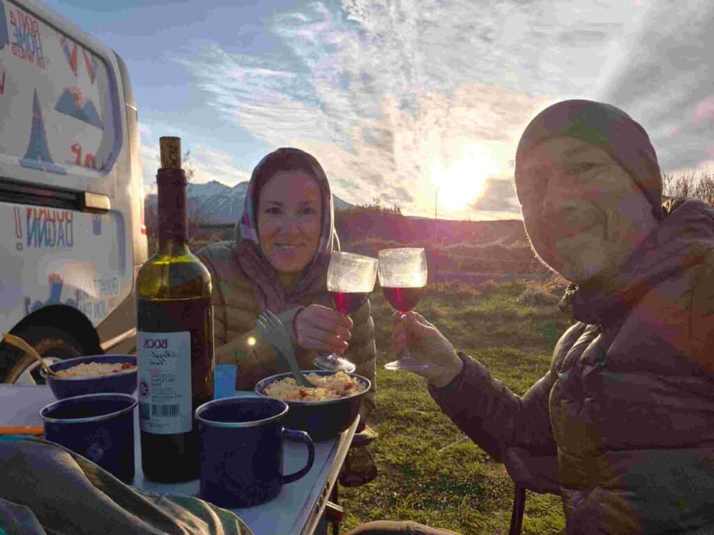 A couple toasting wine glasses with food on the table