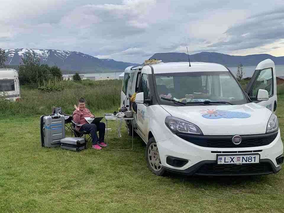 A woman sitting by her Campervan on an unplanned trip in Iceland, working