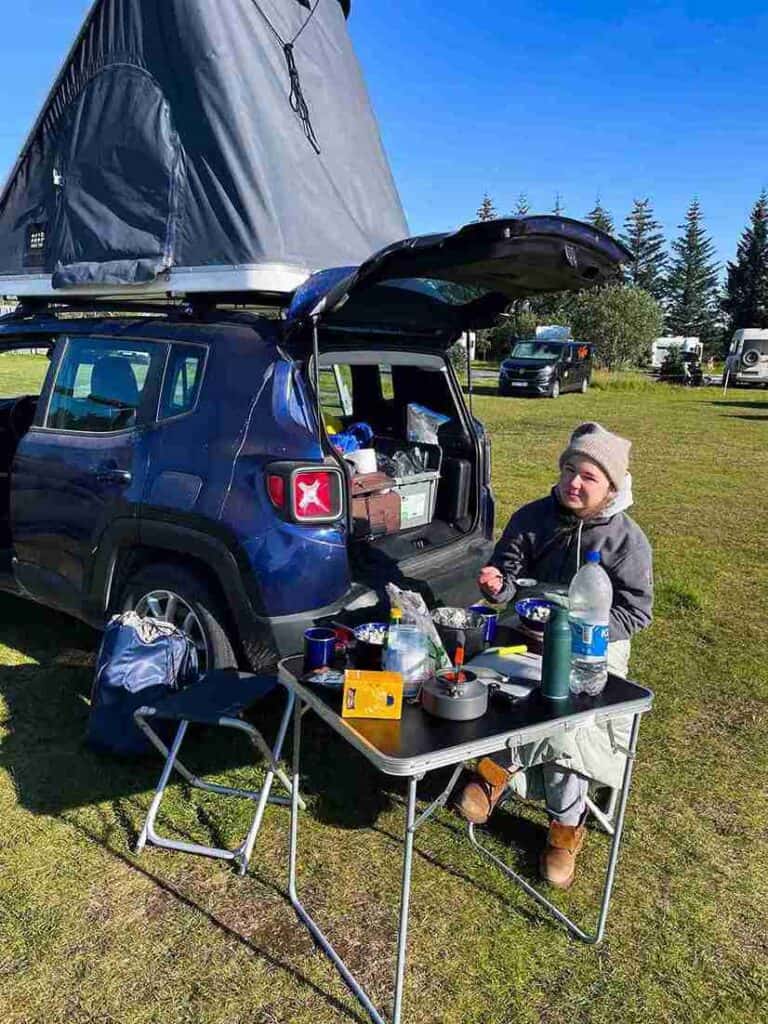 Jeep renegade on a campsite with open trunk, a wild girl sits outside and eats.