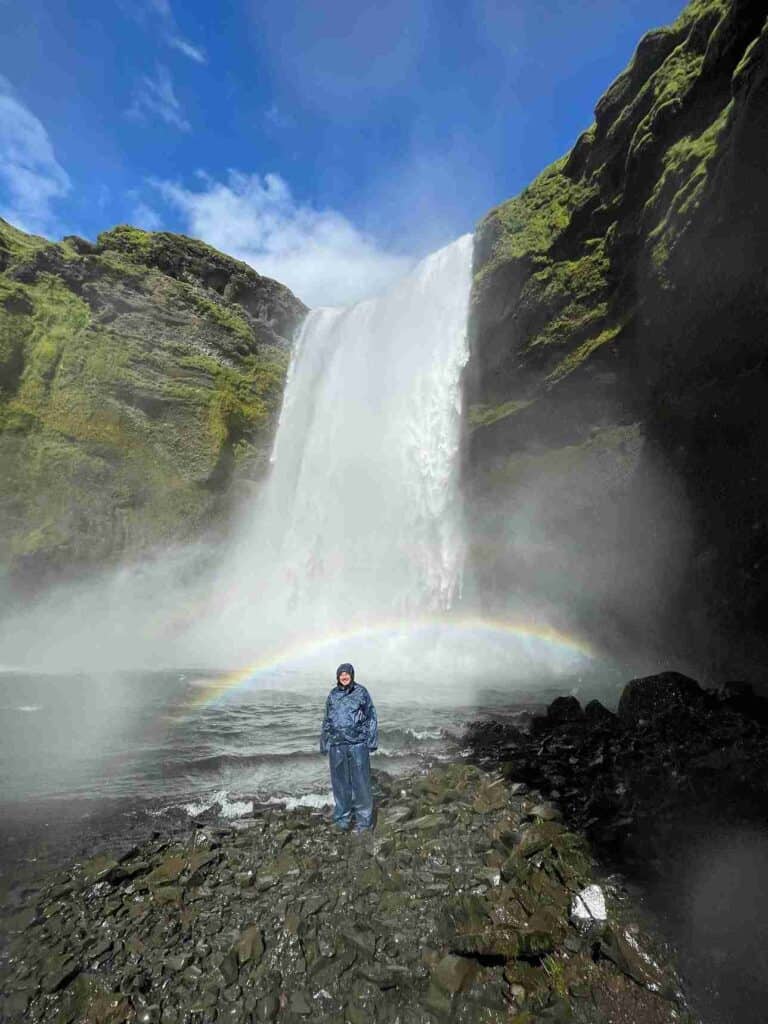 A man standing by a waterfall. A small rainbow there