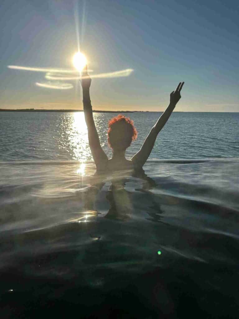 A woman standing in the Sky lagoon looking at the sun set