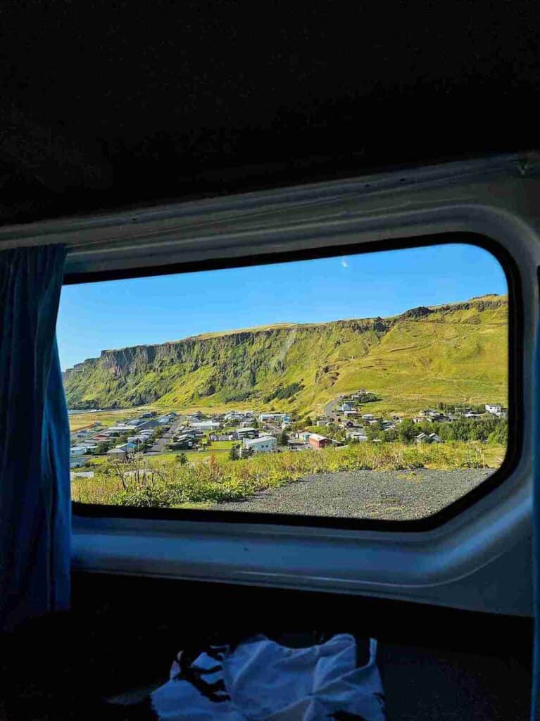 Looking out the side window of a camper trip at a small town in a grassy valley