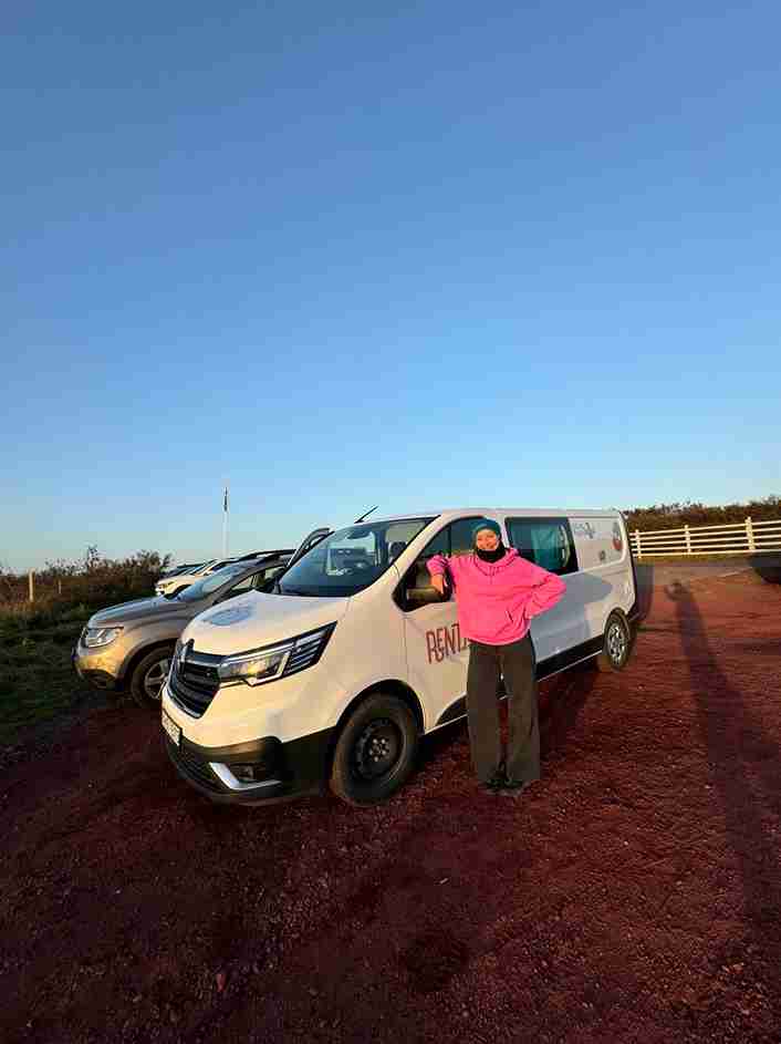 A woman on a trip wearing pink standing by the trafic camper