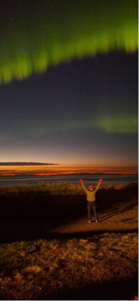 A woman standing on a grassy field by a sunset and Northern lights