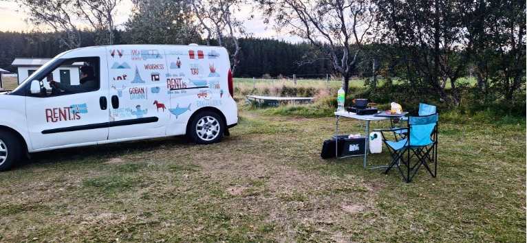 Doblo parked in campsite with camping chairs and table outside