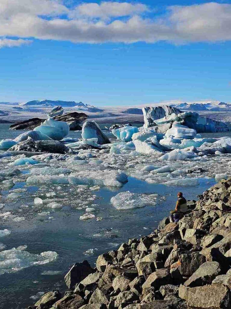 The glacier lagoon, a person sitting on a rock formation watching