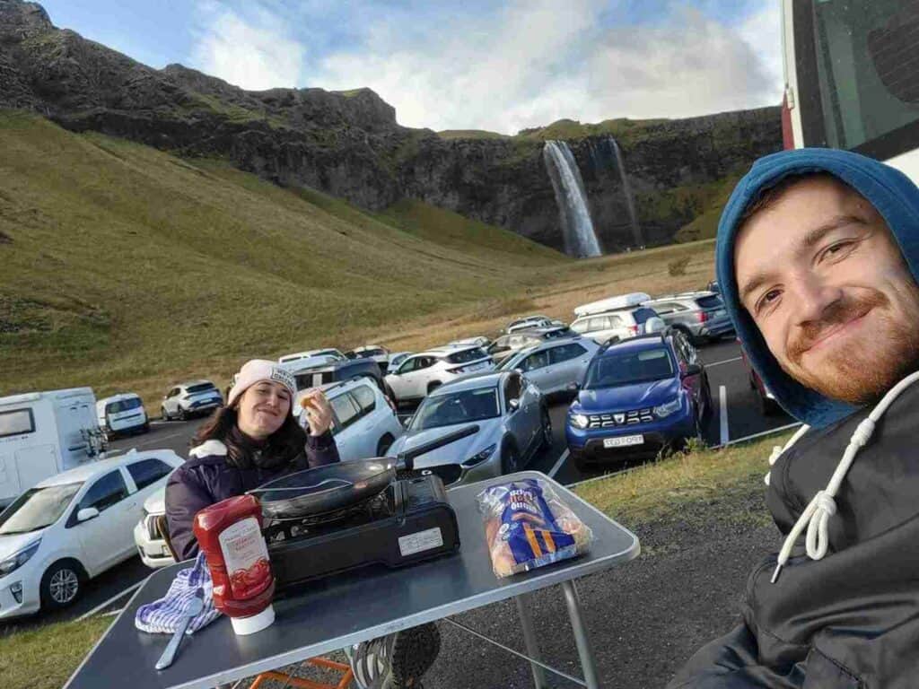 A couple eating hot dogs by a waterfall
