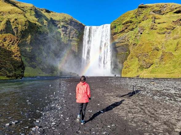 A woman wearing pink standing by skógarfoss, waterfall